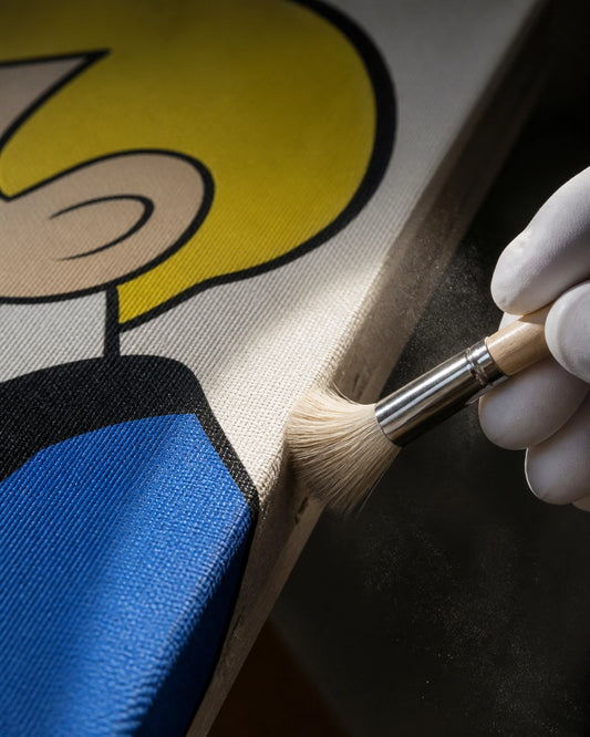 Macro detail of a vibrant pop art canvas corner being gently dusted with a soft conservation brush, with floating dust partic