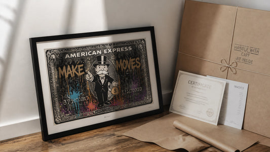 First framed money-art print leaning against a wall on a warm wooden floor beside brown paper, twine, certificate and invoice